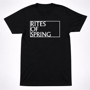 May include: A black short-sleeved t-shirt featuring a white rectangular outline on the chest. Inside the rectangle, the text RITES OF SPRING is printed in a bold, white, serif font, arranged in three stacked lines within the white border frame.