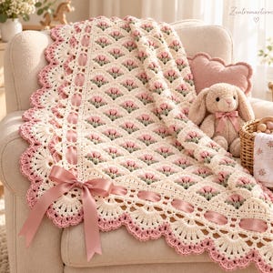 May include: A cream-colored crochet blanket featuring a repeating pattern of small pink tulip motifs with green stems. The border is detailed with a scalloped edge, woven pink satin ribbon, and a large pink satin bow at the corner.