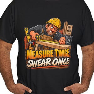 Op de afbeelding: Een zwart t-shirt met een afbeelding van een bouwvakker met een gele helm die een houten plank opmeet met een meetlint. De tekst "MEASURE TWICE SWEAR ONCE" staat in dikke oranje en witte letters, met een klein bordje op de achtergrond.
