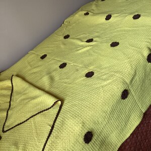 May include: A lime green blanket with dark brown circular accents. The blanket is folded over a bed, with a matching pillow visible. The blanket has a textured weave and a dark brown border.