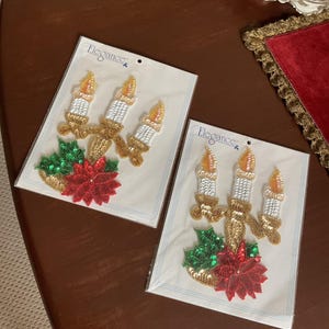 May include: Two packages of Christmas candle appliques. Each applique features three white candles with gold flames, a gold candelabra, green holly leaves, and a red poinsettia. The packages are labeled "Elegance."