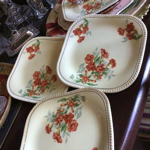 May include: Four square ceramic plates with a cream background and a floral design featuring red trumpet-shaped flowers with green leaves.