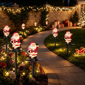 Pode incluir: Um conjunto de estacas solares para jardim com figuras iluminadas de Pai Natal. Cada Pai Natal veste um fato vermelho e branco, segura uma bengala doce e está montado num poste preto. As figuras emitem uma luz quente ao longo do caminho.