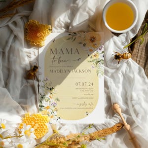 Op de afbeelding: Een gele en witte bloemachtige babyshower-uitnodiging met de tekst "Mama to be" en "Madelyn Jackson". De uitnodiging bevat ook de datum "07.07.24" en de tijd "13:00 uur".