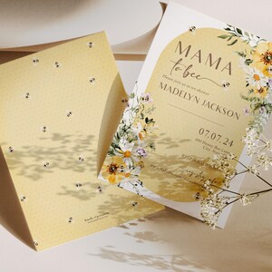 Op de afbeelding: Een gele en witte babyshower-uitnodiging met een bloemenontwerp en de tekst "Mama to bee" en "Madelyn Jackson". De uitnodiging bevat ook de datum "07.07.24" en het adres "100 Honey Bee Lane, City, State".