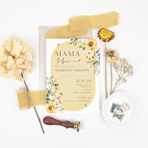 Op de afbeelding: Een gele en witte bloemige babyshower-uitnodiging met de tekst "Mama to bee" en de naam "Madelyn Jackson". De uitnodiging heeft een aquarel-bloemendesign met bijen en een datum van 07.07.24.