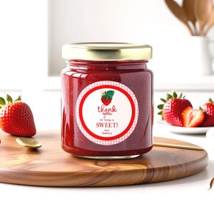 May include: A jar of strawberry jam with a gold lid and a label that reads "thank you for being so SWEET!" with a strawberry illustration. Fresh strawberries are arranged around the jar on a wooden cutting board.
