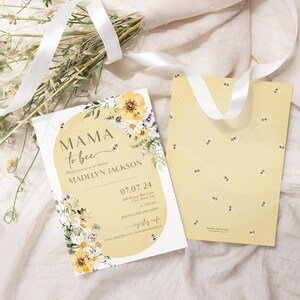 Op de afbeelding: Een gele en witte bloemige babyshower-uitnodiging met de tekst "Mama to Bee" en de naam "Madelyn Jackson". De uitnodiging heeft een bijenpatroon en een datum van 07.07.24.