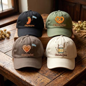 May include: Four baseball caps in black, olive green, brown, and cream, each featuring an Oktoberfest graphic. The black cap shows a sausage with a flag, the green cap a pretzel, the brown cap a heart cookie, and the cream cap a beer mug.