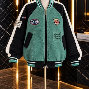 May include: A black and green sherpa bomber jacket with a front zipper, striped ribbed collar, cuffs, and hem. The jacket features various embroidered patches, including text reading JAJE-7TH and RUNNING KOWARDS SLOMA85 BECMLY10 on the front.