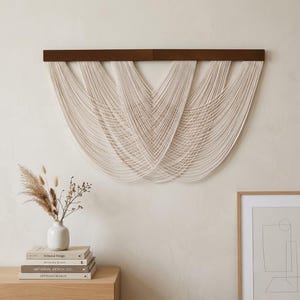 May include: A wall hanging featuring a horizontal dark brown wooden bar with multiple off-white cotton cords draped in a series of overlapping, cascading U-shaped loops that create a layered, symmetrical, and rhythmic pattern across the wall.