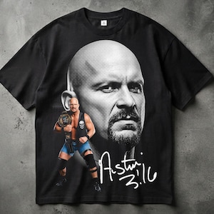 Puede incluir: Una camiseta negra de manga corta con un gran retrato en escala de grises de un hombre calvo con perilla. Debajo del retrato hay una imagen de cuerpo entero del mismo hombre con equipo de lucha libre sosteniendo un cinturón de campeón, con el texto Austin 3:16 en blanco.