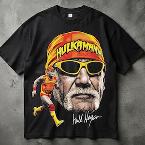 Puede incluir: Una camiseta negra de manga corta con un gran estampado gráfico de Hulk Hogan con un pañuelo amarillo con el texto HULKAMANIA y gafas de sol amarillas. Se incluye una imagen más pequeña del luchador y la firma de Hulk Hogan.