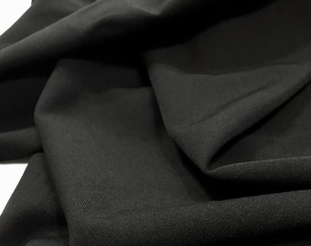 Può includere: Tessuto nero con una superficie liscia e leggermente strutturata. Il tessuto è piegato e drappeggiato, mostrando la sua natura morbida e fluida.