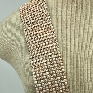 May include: A long strip of rose gold coloured rhinestone trim. The trim is made of small square rhinestones that are sewn together in a grid pattern.
