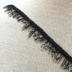 May include: Black lace trim with dangling clear beads. The trim is made of a delicate, open weave material. The beads are small and evenly spaced along the fringe. This trim is suitable for various craft and sewing projects.