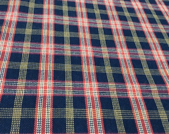 May include: Close-up of a plaid fabric with a repeating pattern of navy blue, red, white, and yellow lines. The fabric has a textured appearance, with the lines intersecting to create a grid-like design. The overall effect is a classic, timeless look.