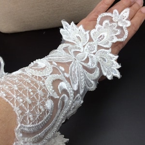 Op de afbeelding: Witte kantversiering met parelversiering. De kant heeft een bloemmotief met delicate bladeren en ingewikkelde details.