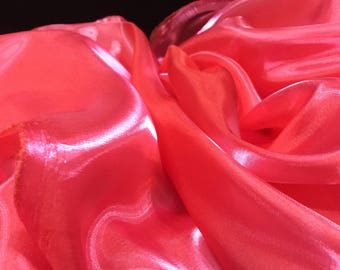 May include: A close-up of a bright pink satin fabric with a smooth, shiny texture. The fabric is draped and folded, creating soft, flowing curves.