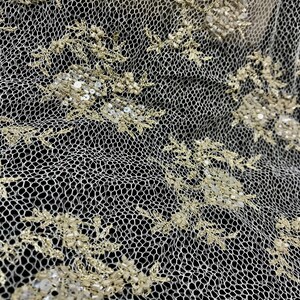 K&ouml;nnte beinhalten: Nahaufnahme eines elfenbeinfarbenen Spitzenstoffs mit aufwendiger floraler Stickerei. Das filigrane Design weist kleine, schimmernde Pailletten und Perlen auf, die ein strukturiertes und elegantes Aussehen erzeugen. Die Spitze ist vor einem dunklen Hintergrund platziert, der das detaillierte Muster hervorhebt.