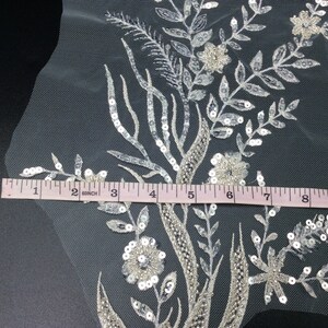 Può includere: Ricamo floreale bianco con paillettes e perline su un tessuto di tulle trasparente. Il ricamo misura 9 pollici di larghezza.