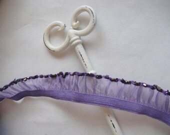 Peut inclure: Garniture à volants violette avec des perles irisées. La garniture est présentée avec une clé décorative blanche.