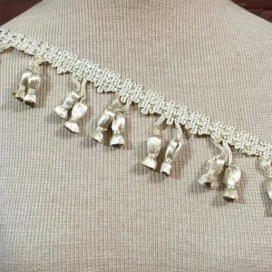 Peut inclure: Gros plan d'une garniture blanche avec une frange de glands. La garniture est faite d'un tissu d&eacute;licat et tiss&eacute; et a un l&eacute;ger &eacute;clat.