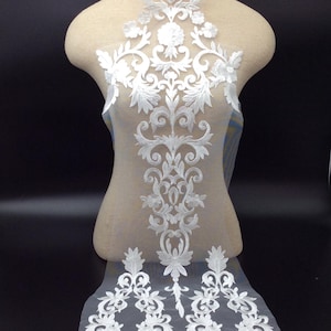 May include: White lace applique featuring a floral design. The lace is delicate and intricate, with a variety of floral motifs. The applique is ideal for adding a touch of elegance to any garment.