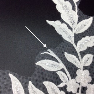 May include: White embroidered lace fabric with a floral design. The lace features delicate leaves and flowers with small, sparkling embellishments.