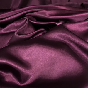 May include: A close-up of a smooth, deep purple satin fabric. The fabric is draped and folded, creating soft, flowing lines.