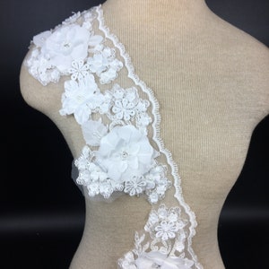 May include: White lace trim with 3D floral embellishments. The trim features delicate lacework and large, raised flowers with pearl accents.