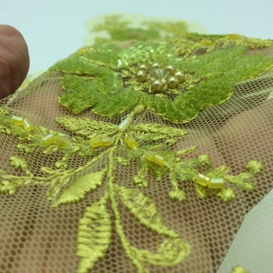 May include: Yellow floral embroidery with green leaves and beads on a sheer mesh fabric.
