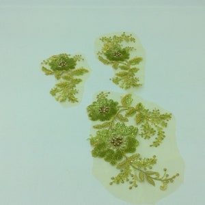 May include: Three floral appliques with green and gold embroidery. The appliques feature detailed flower and leaf designs with beaded accents. The appliques are on a cream-colored mesh backing, suitable for embellishing garments or crafts.