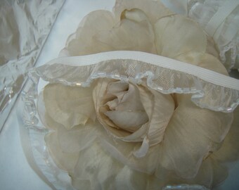 Peut inclure: Une fleur en tissu blanc avec une bordure en dentelle blanche et un élastique blanc.