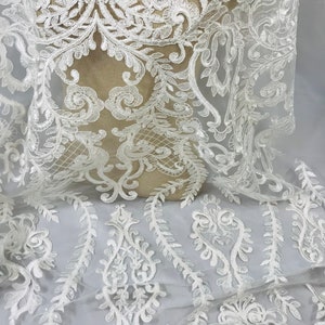 Op de afbeelding: Witte kantstof met een delicaat bloemenpatroon. De kant heeft een subtiele glans en is perfect om een ​​toets van elegantie aan elk project toe te voegen.