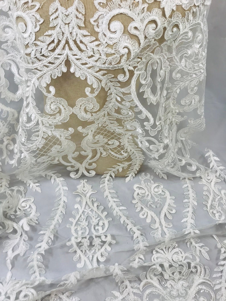 Op de afbeelding: Witte kantstof met een delicaat bloemenpatroon. De kant heeft een subtiele glans en is perfect om een ​​toets van elegantie aan elk project toe te voegen.