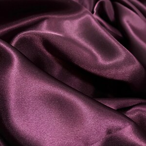 May include: Close-up of a deep purple satin fabric with soft, flowing folds and a smooth, silky texture.