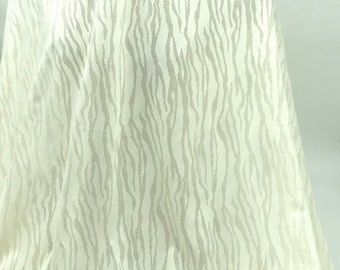 May include: Off-white fabric with a textured pattern of vertical, wavy lines in a lighter shade. The fabric is draped, showing folds and a soft, flowing appearance. The overall effect is subtle and elegant.