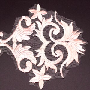 Op de afbeelding: Witte geborduurde kant applique met een bloemenmotief. De kant is delicaat en ingewikkeld, met een wervelend patroon van bladeren en bloemen. De applique is perfect om een ​​toets van elegantie aan elk project toe te voegen.