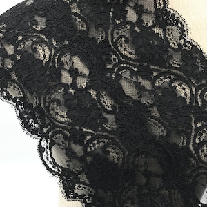 May include: Black lace trim featuring a delicate floral design. The lace is soft and has a scalloped edge.