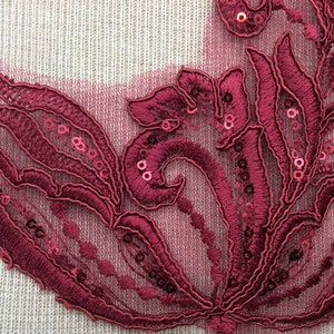 Peut inclure: Applique en dentelle bordeaux avec des paillettes, présentant un motif floral. L'applique est délicate et complexe, avec une texture douce et fluide.