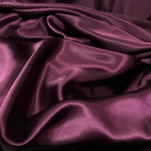 May include: A close-up of a deep purple satin fabric, showing the smooth, silky texture and the way the fabric drapes and folds.