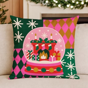 May include: A square throw pillow featuring a central snow globe graphic with a red fireplace, stockings, and gifts. The background is divided into four quadrants with alternating patterns of white snowflakes on dark green and pink and gold diamonds.