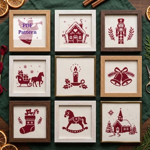 May include: Nine square frames containing cross-stitch embroidery on white fabric. The designs are in dark red and feature an angel, gingerbread house, nutcracker, sleigh, candle, bells, stocking, rocking horse, and church. Text reads PDF Pattern.