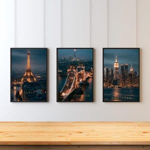 May include: Three vertical framed wall art prints featuring night cityscapes of Paris with the Eiffel Tower, London with Tower Bridge, and New York with the Empire State Building. Each print includes the city name in gold text at the bottom.