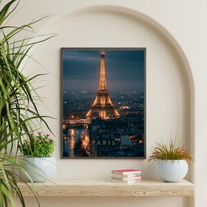May include: A rectangular wall art print featuring a night view of the Eiffel Tower in Paris, illuminated with warm golden lights against a dark blue twilight sky, with the word PARIS printed in gold capital letters at the bottom centre.