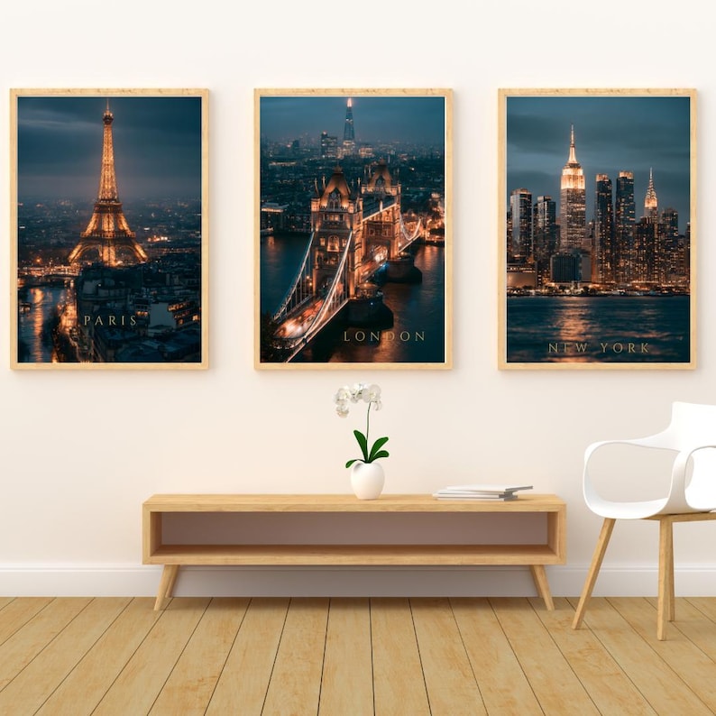 May include: Three vertical framed wall art prints featuring night cityscapes of Paris, London, and New York. Each print displays illuminated landmarks including the Eiffel Tower, Tower Bridge, and the New York skyline with the text labels PARIS, LONDON, and NEW YORK.