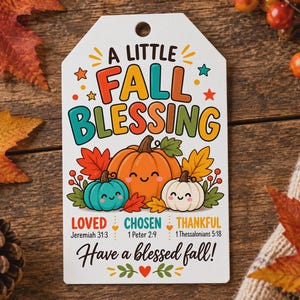 Op de afbeelding: Een wit rechthoekig cadeaulabel met een gat aan de bovenkant, voorzien van de tekst A LITTLE FALL BLESSING in kleurrijke letters. Daaronder staan drie cartoonpompoenen in oranje, groenblauw en wit, met de woorden LOVED, CHOSEN en THANKFUL.