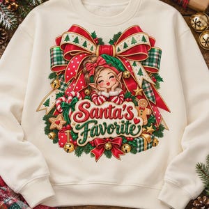 May include: A cream-colored crewneck sweatshirt featuring a graphic print of a cartoon elf with a large red bow, candy canes, gingerbread cookies, and gift boxes. The text "Santa's Favorite" is written in red and green script in the center.