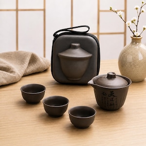 Peut inclure: Un service à thé en céramique marron foncé comprenant un gaiwan avec couvercle orné de calligraphies chinoises noires, trois petites tasses assorties et un étui de transport carré zippé avec une forme moulée épousant le gaiwan.